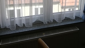 A window with sheer curtains, a view of a brick building, and a vent below the window. - Gästehaus Heigeleshof (Ulm)