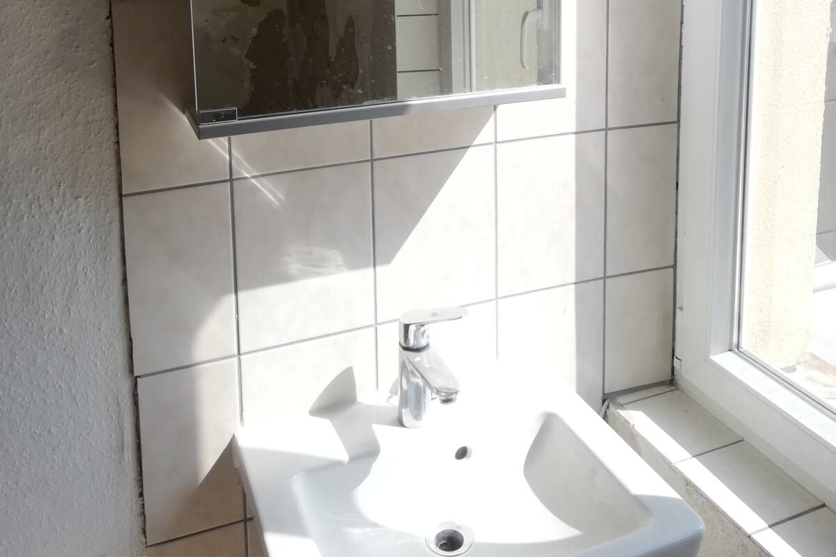 A bathroom with a white sink, a mirror, and a window.