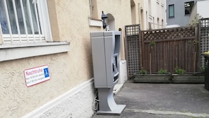 A narrow alley with a wooden planter box containing purple and white flowers, a water dispenser, and a sign indicating restricted access hours. - Gästehaus Heigeleshof (Ulm)