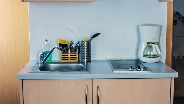 A compact kitchenette with a sink, a coffee maker, and a small countertop. - Gästehaus Heigeleshof (Ulm)