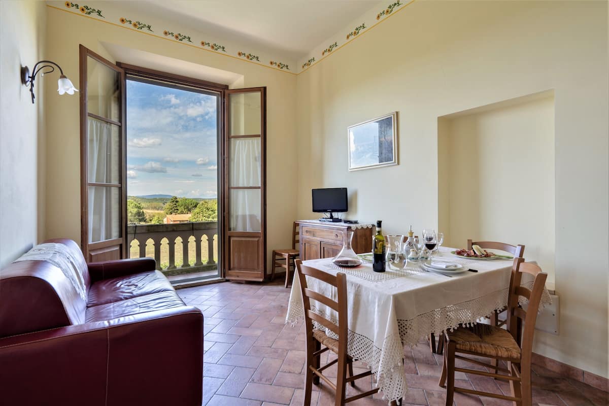 Un coin repas avec une table dressée pour deux personnes, un téléviseur et une vue sur la campagne.