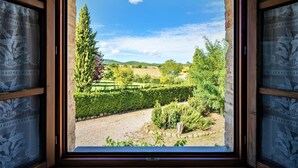 Blick aus dem Fenster auf einen Garten mit ordentlich geschnittenen Hecken, einem Kiesweg und verschiedenen Bäumen.
