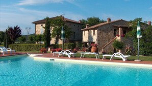Ein Pool mit Liegestühlen und ein Steinhaus im Hintergrund.