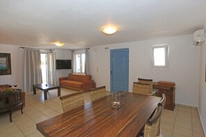 A spacious living area with a wooden dining table, a sofa, and a television. - Sunrise Beach Suites (Syros)
