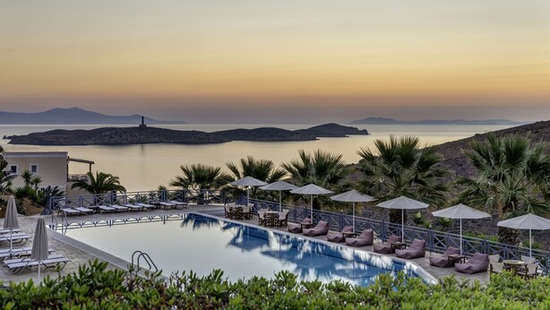 A pool area with lounge chairs and umbrellas, overlooking a calm body of water and distant islands. - Sunrise Beach Suites (Syros)