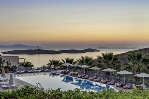 A pool area with lounge chairs and umbrellas, overlooking a calm body of water and distant islands. - Sunrise Beach Suites (Syros)