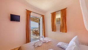 A hotel room with a bed, a TV, and a view of the sea. - Sunrise Beach Suites (Syros)