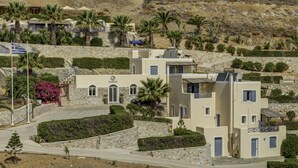 A modern building with a stone facade, multiple balconies, and a flag. - Sunrise Beach Suites (Syros)