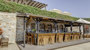 An outdoor bar with stone walls, wooden bar stools, and umbrellas. - Sunrise Beach Suites (Syros)