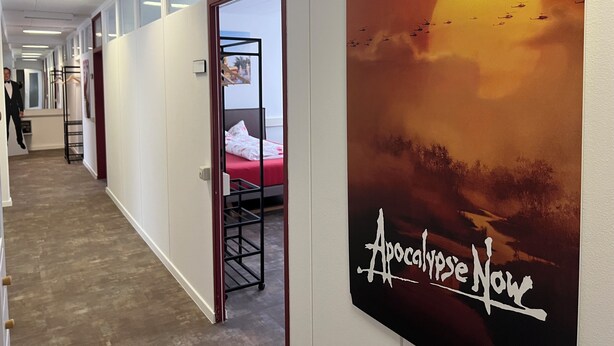 A hallway with a bed, a wardrobe, and a painting of a sunset. - Boot Camp Central - Hostel (Friedrichshafen)