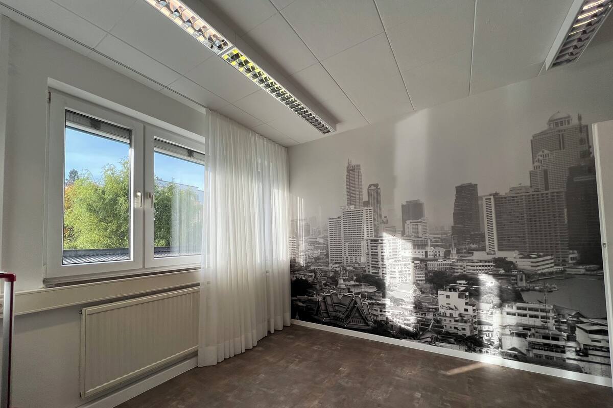 A room with a large window, a radiator, and a cityscape mural on the wall.