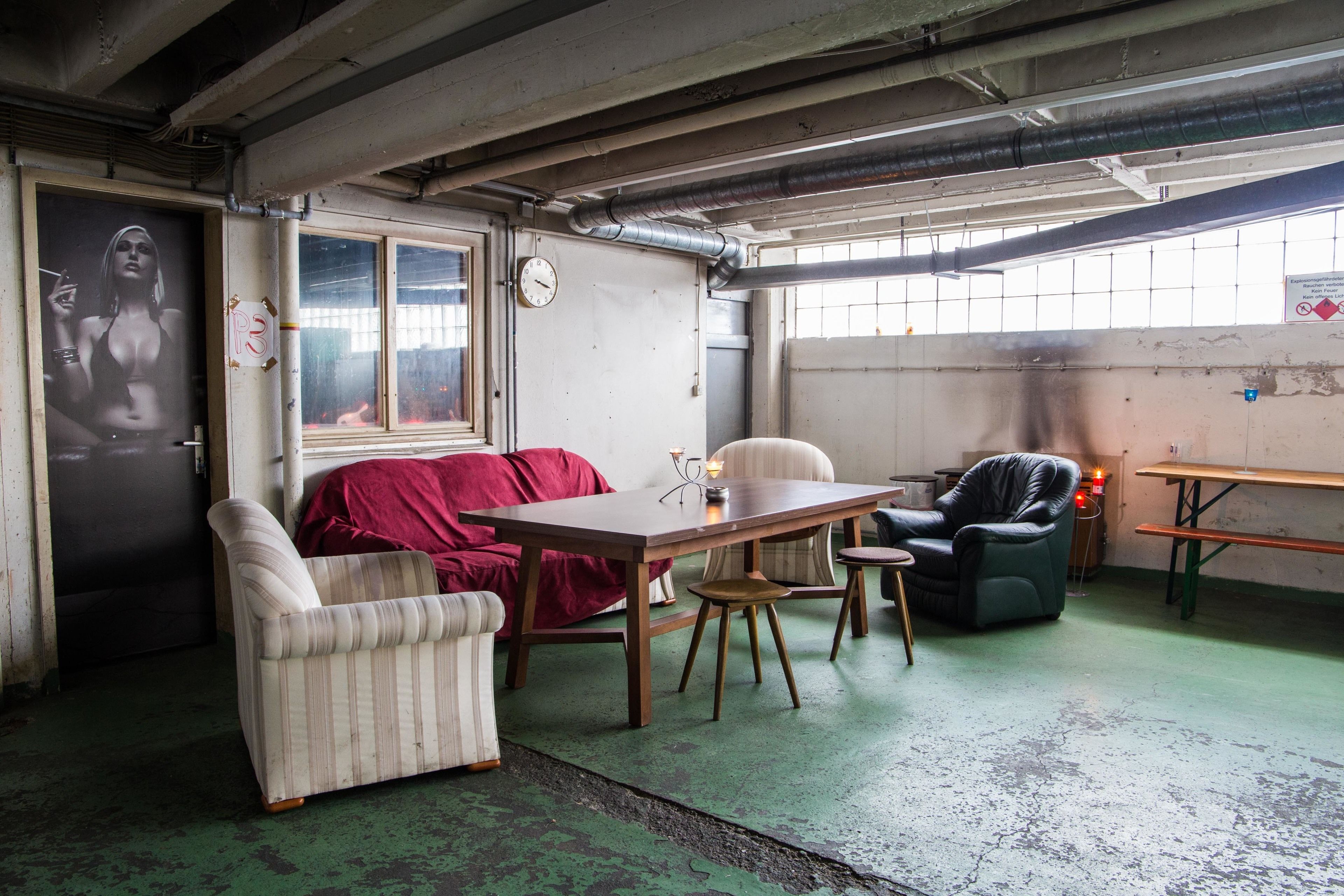 A room with a sofa, a table, and a chair. There is a clock on the wall and a window with a view outside.
