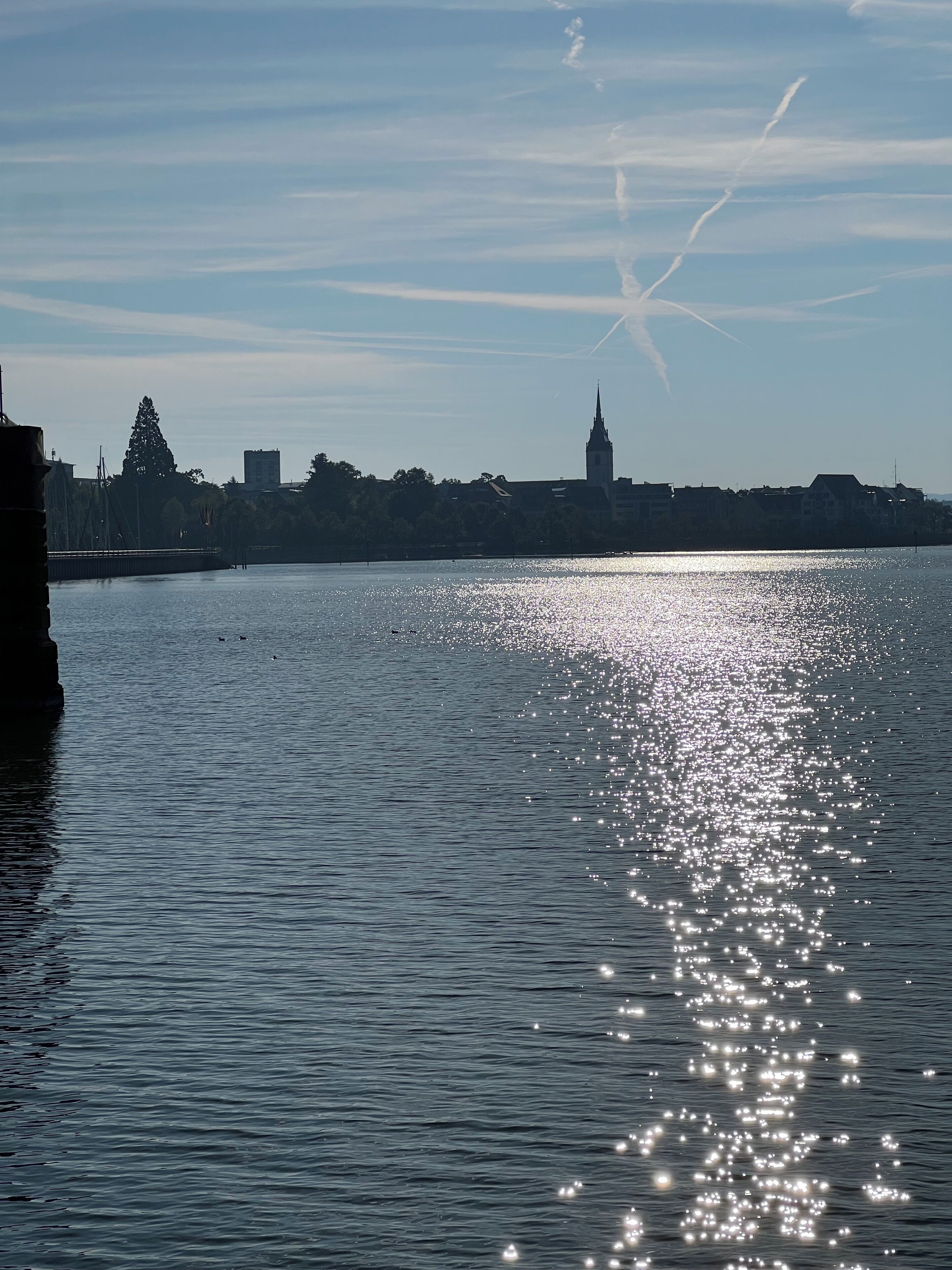 Un río tranquilo reflejando la luz del sol con un horizonte lejano de la ciudad, incluyendo una alta aguja de iglesia.