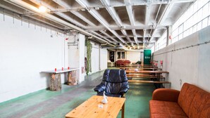 A spacious indoor area with a green floor, wooden tables, a leather chair, and an orange sofa. - Boot Camp Central - Hostel (Friedrichshafen)