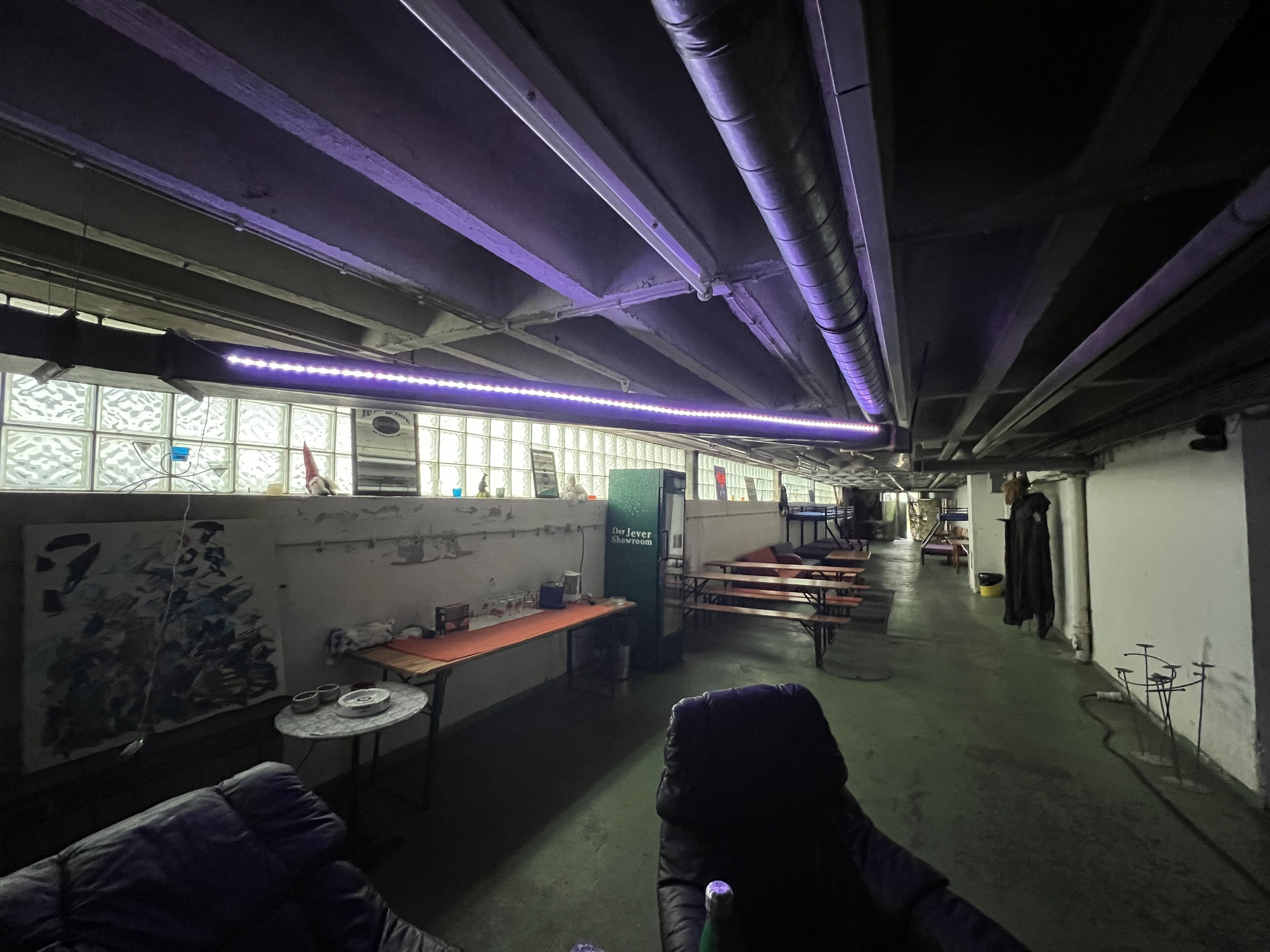 Une pièce faiblement éclairée, avec un éclairage violet, une fenêtre à vitres décorées, une table avec une chaise et un canapé.