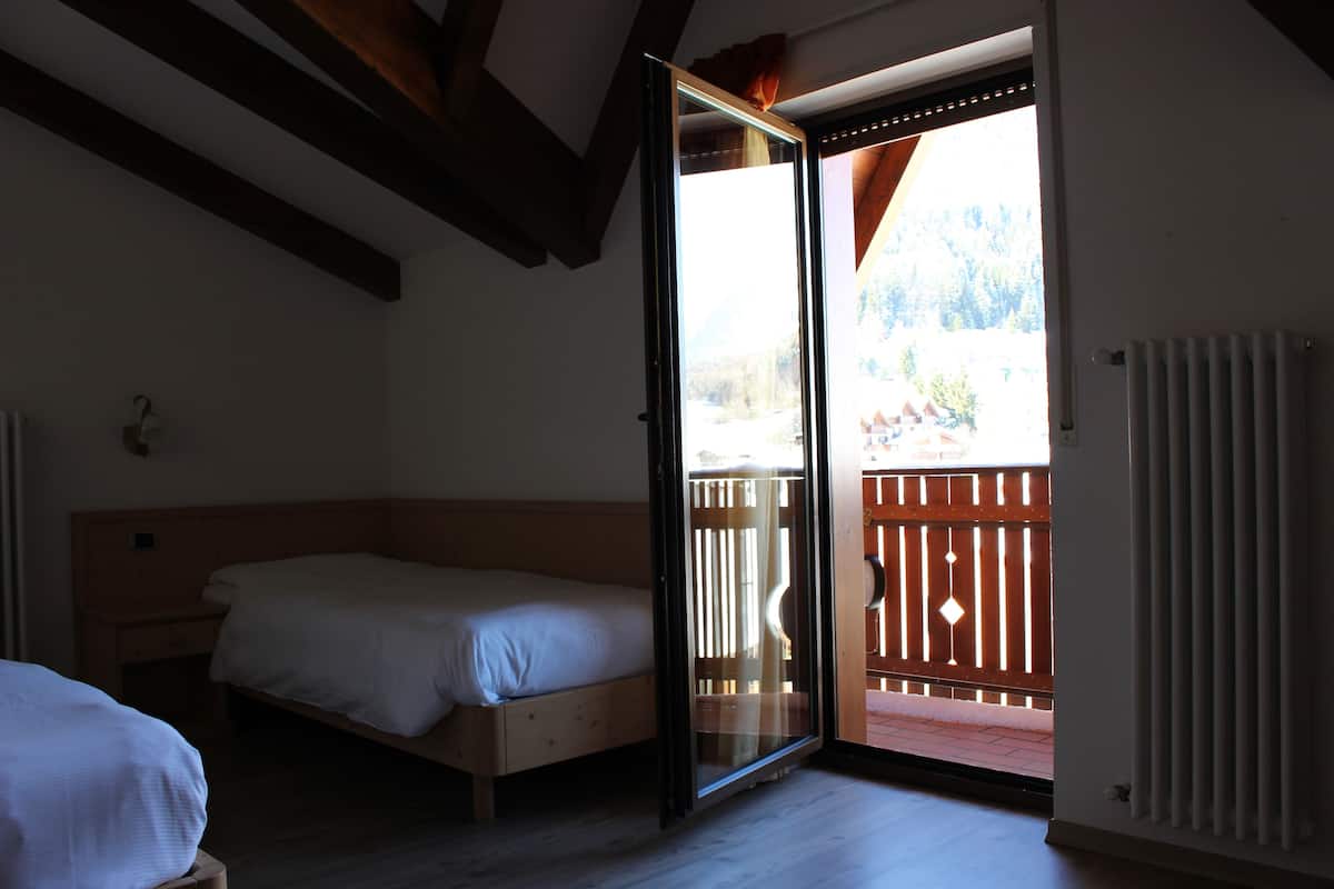 Una habitación con dos camas, vigas de madera en el techo y un ventanal corredero que da a un área exterior con valla de madera.