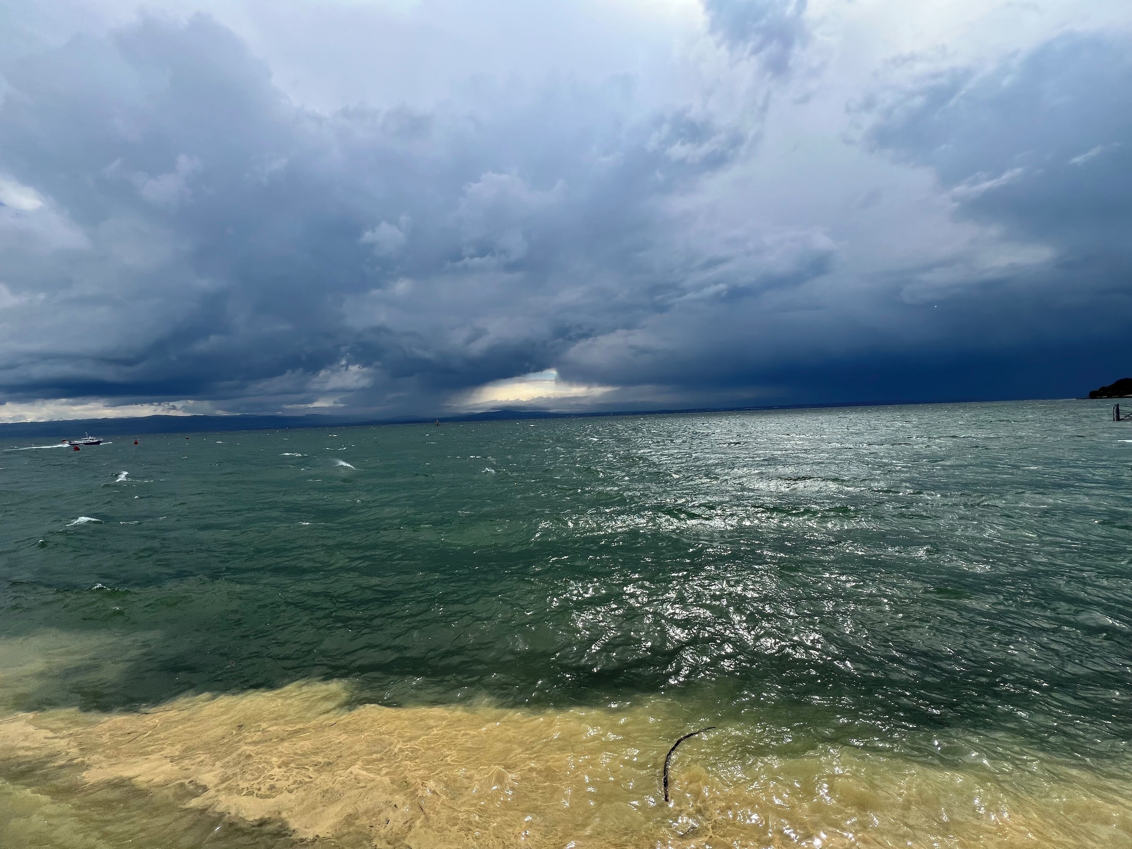 Una playa con agua cristalina, un barco a lo lejos y un cielo nublado.