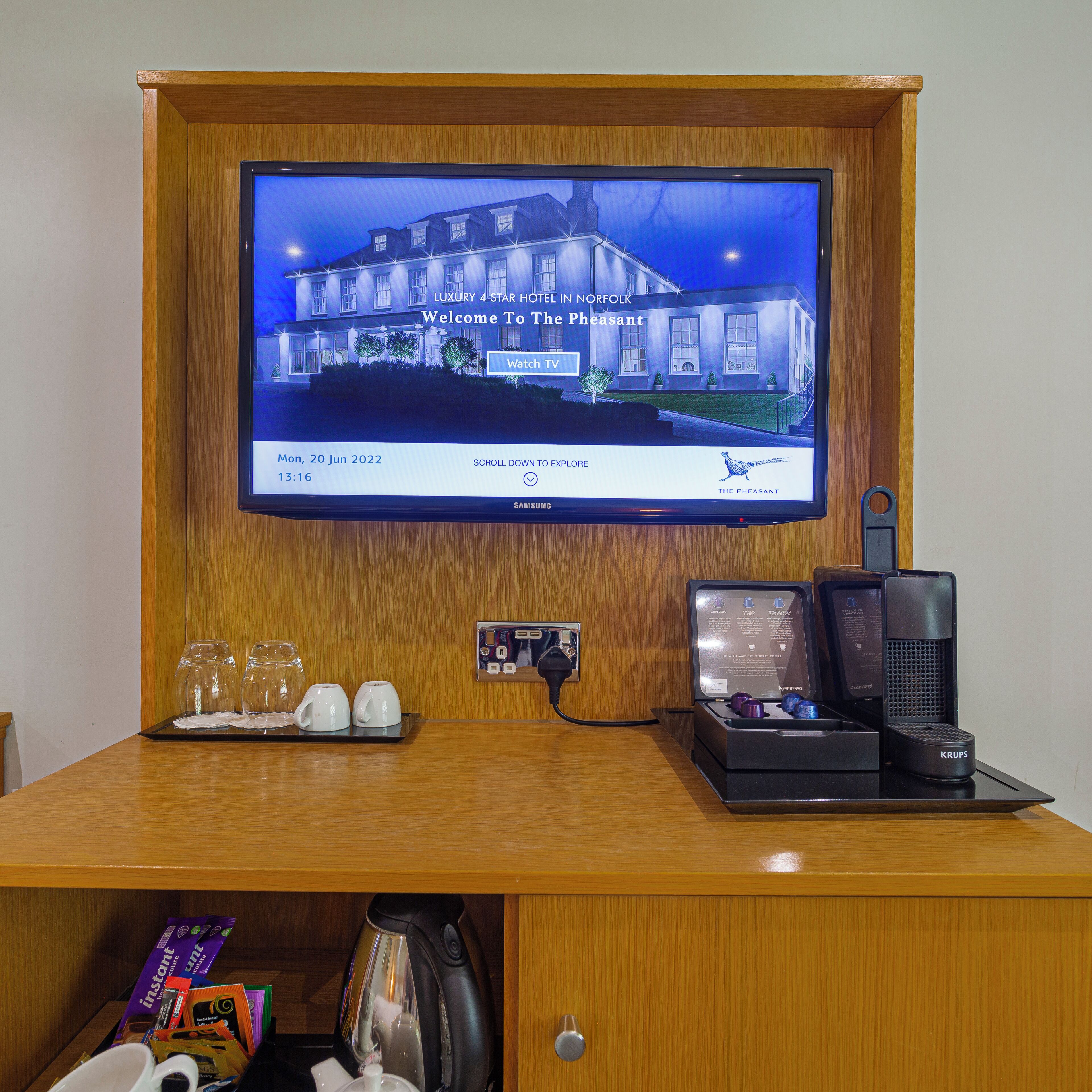A hotel desk with a TV displaying a property image, a coffee machine, and a kettle.