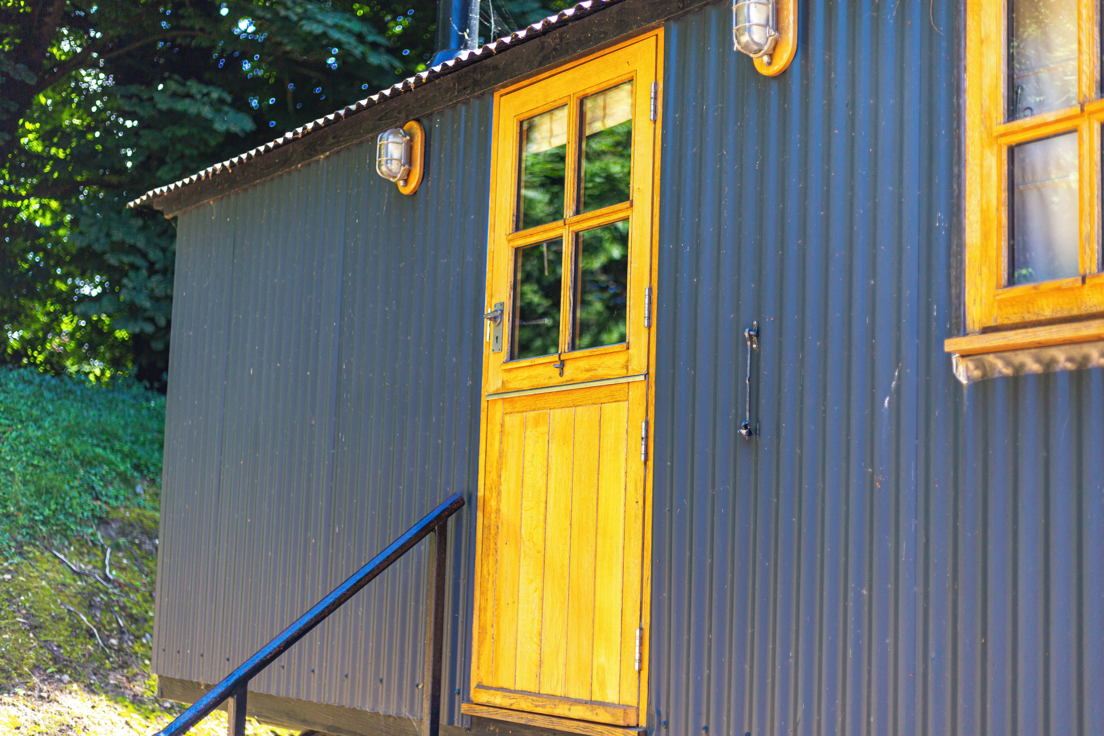 A small, single-story building with a wooden door and windows, a metal roof, and a blue exterior.