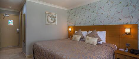 A hotel room with a large bed, a wooden headboard, a nightstand, and a wall-mounted lamp.