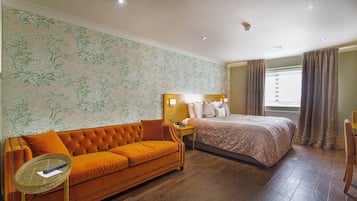 Una habitación de hotel con una cama grande, un sofá naranja, una mesita pequeña y una ventana con cortinas.