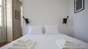 A neatly made bed with white linens and towels, two wall-mounted lamps, and a framed picture on the wall. - Liiiving In Porto - Central Secret Balcony (Porto)