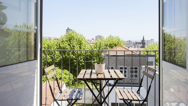 A balcony with a wooden table and chairs, a potted plant, and a city view. - Liiiving In Porto - Central Secret Balcony (Porto)