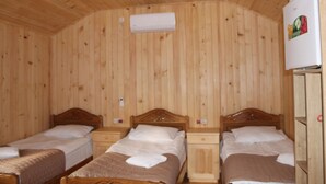 A wooden-paneled room with two wooden beds, a white air conditioner, and a white refrigerator with a colorful sticker.