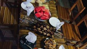 A long wooden table set for a meal with various dishes, including watermelon, bread, and a bottle of Coca-Cola.