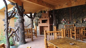 Un área de comedor al aire libre con mesas y sillas de madera, un muro de piedra y un horno de ladrillo.