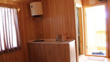 Interior de una cabaña de madera con kitchenette, una ventana con cortinas y una puerta que da al exterior.