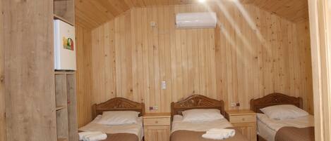 Une pièce aux murs lambrés, avec trois lits en bois, un climatiseur blanc et un luminaire fixé au plafond.