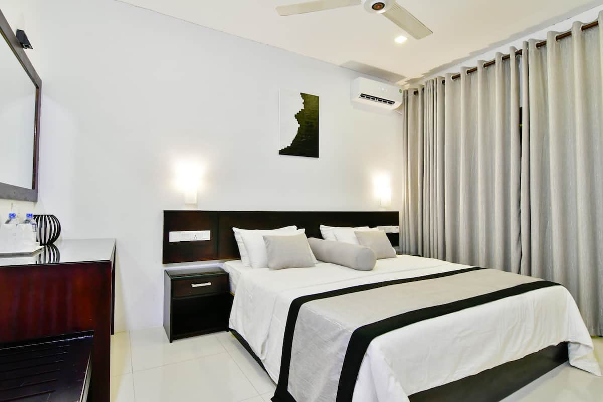 A hotel room with a large bed, a desk, a nightstand, a wall-mounted air conditioner, and a ceiling fan.