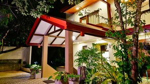 A two-story building with a covered outdoor area, potted plants, and a staircase.