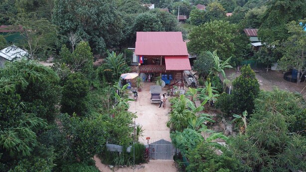 A house with a red roof surrounded by dense greenery. - Authentic Cambodian Angkor Cottage (Siem Reap)