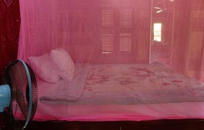 Una cama con mosquitero, ventilador y colcha estampada.