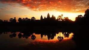 A sunset over a temple complex with reflections in a body of water. - Authentic Cambodian Angkor Cottage (Siem Reap)