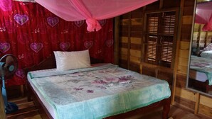 A wooden bed with a floral bedspread, a standing fan, and a red curtain with heart patterns. - Authentic Cambodian Angkor Cottage (Siem Reap)