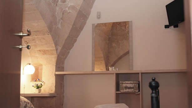 Un dormitorio con un arco de piedra, una cama con toallas enrolladas, una lámpara de noche, un espejo y un televisor en la pared.