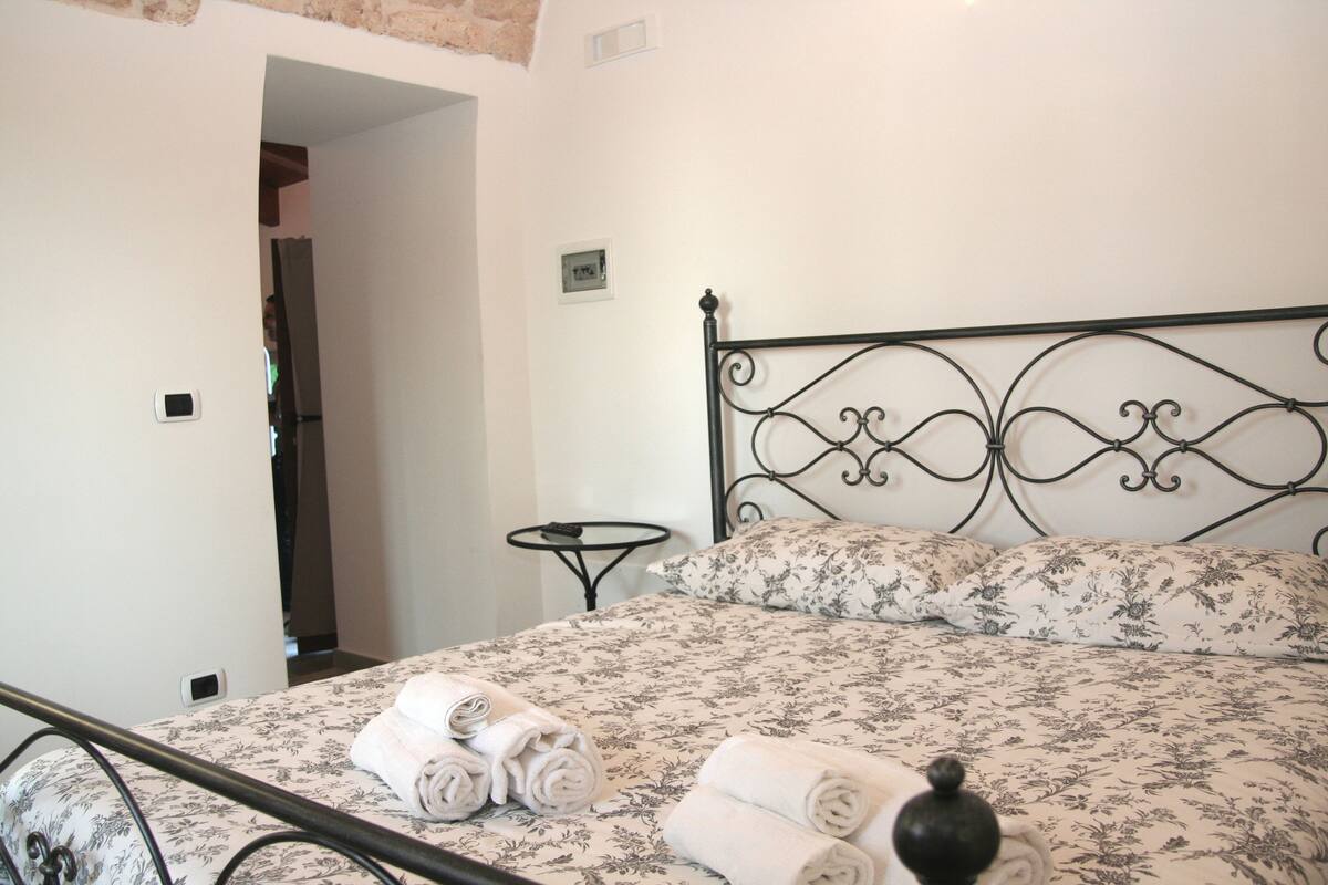 A neatly made bed with floral bedding, a small bedside table, and a wall-mounted light fixture.