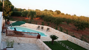 Una piscina de piedra con sillones de descanso, una terraza de madera y vistas del paisaje circundante.