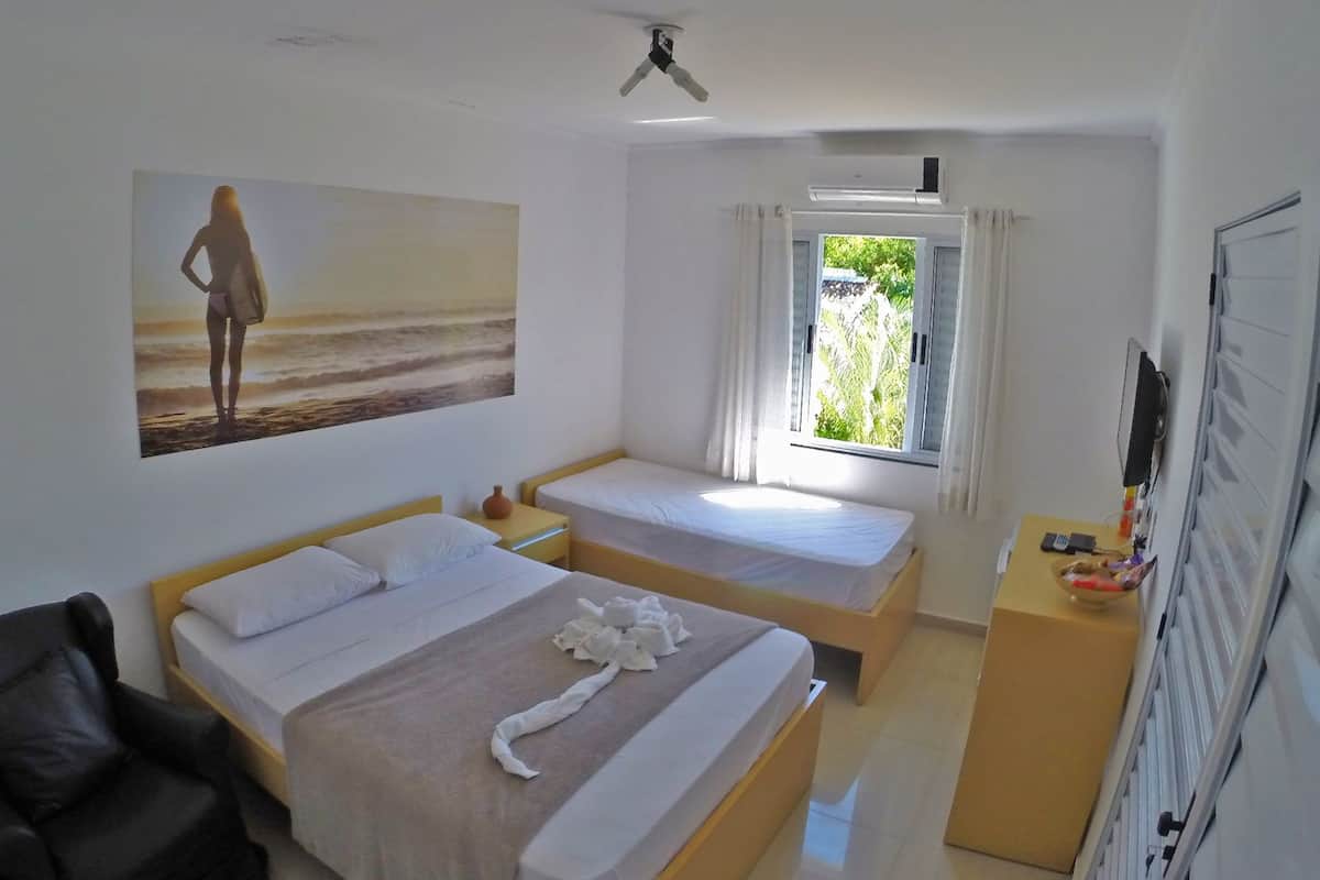 Ein Hotelzimmer mit zwei Betten, einem Schreibtisch, einem Stuhl, einem Bild von einer Strandansicht und einem Fenster mit Vorhängen.