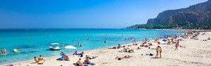 A crowded beach with clear blue water, people sunbathing, and boats. - Home Beach Mondello Galatea (Palermo)