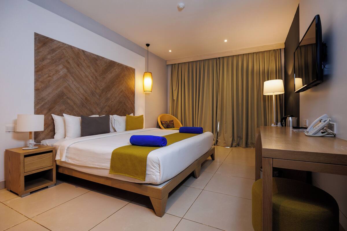 A hotel room with a large bed, bedside tables, a desk, a chair, a mirror, and a telephone.