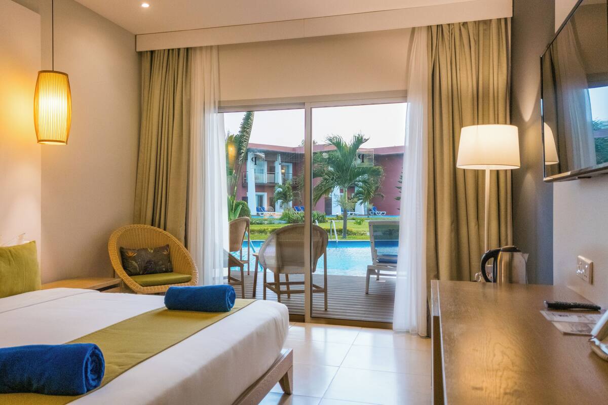 A hotel room with a bed, a chair, a desk, a television, and a view of a pool and building outside.