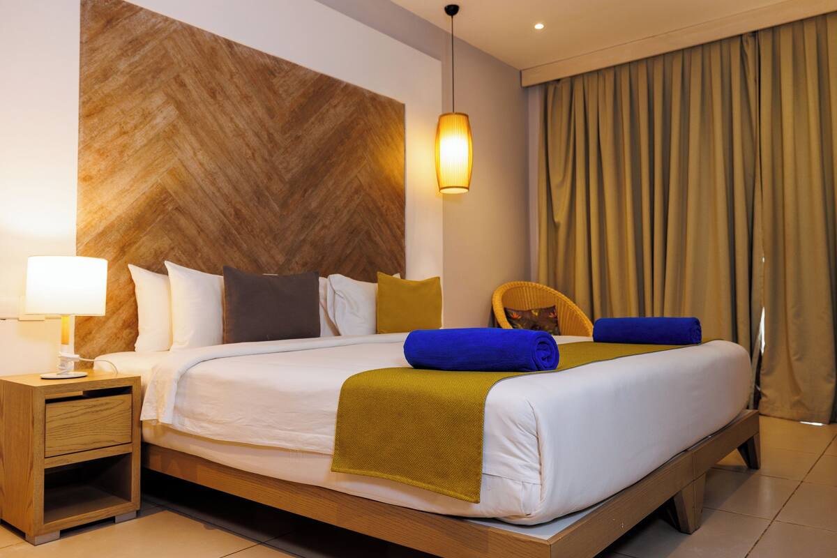 A hotel room with a large bed, a nightstand, a lamp, and a wooden headboard.