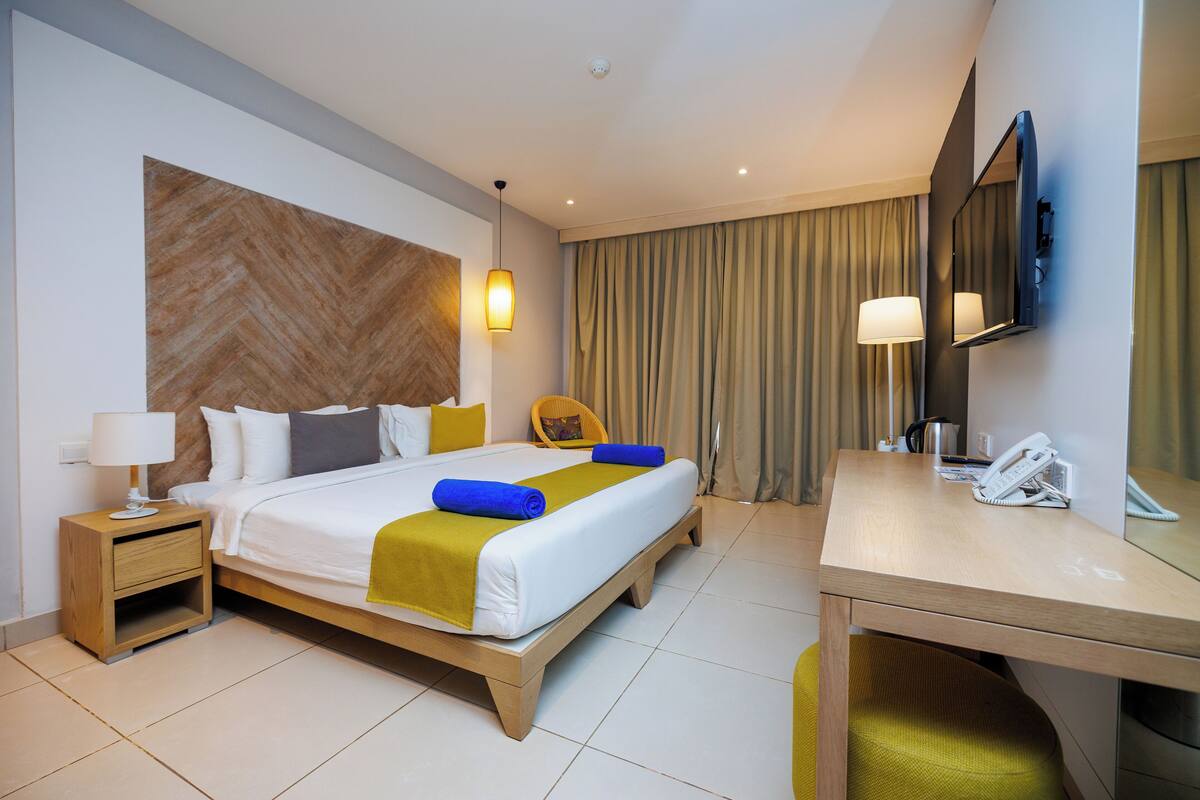A hotel room with a bed, bedside table, lamp, chair, desk, and a telephone.