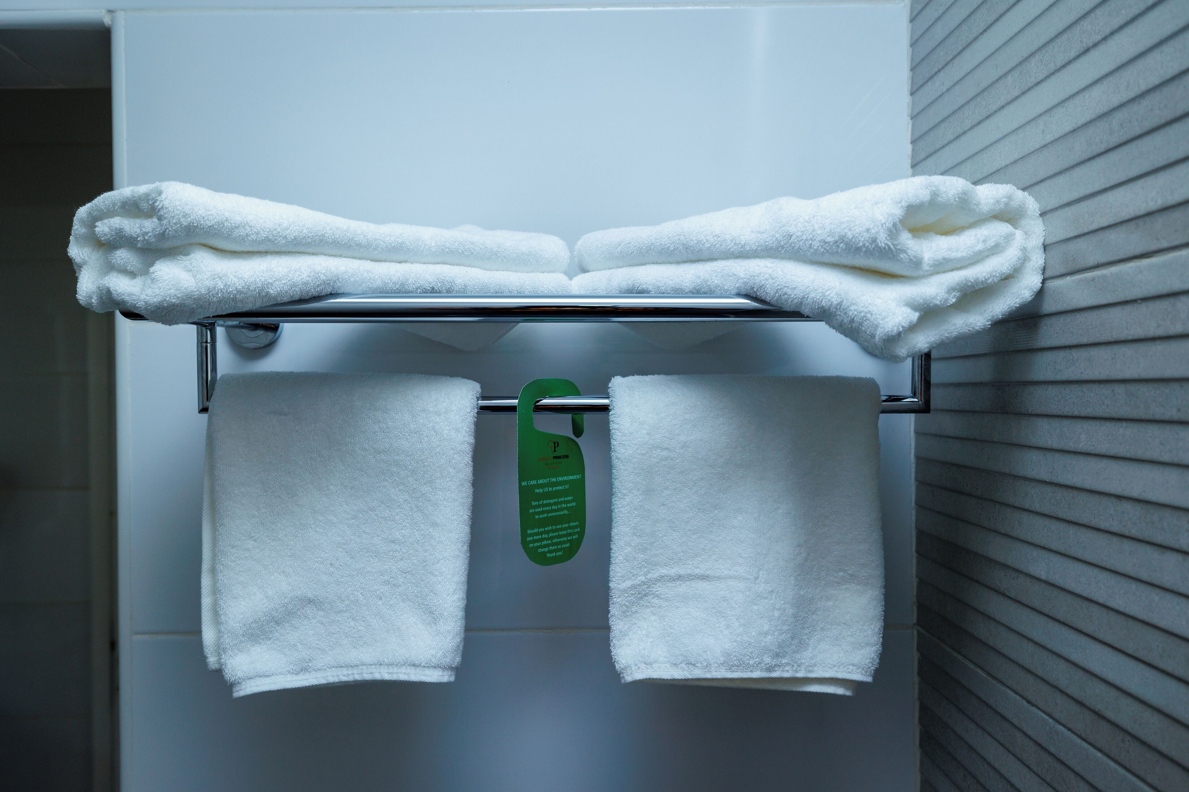 Un baño con un perchero que sostiene dos toallas dobladas y un cartel verde.