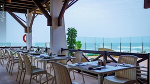 An outdoor dining area with wicker chairs and tables, overlooking the ocean.