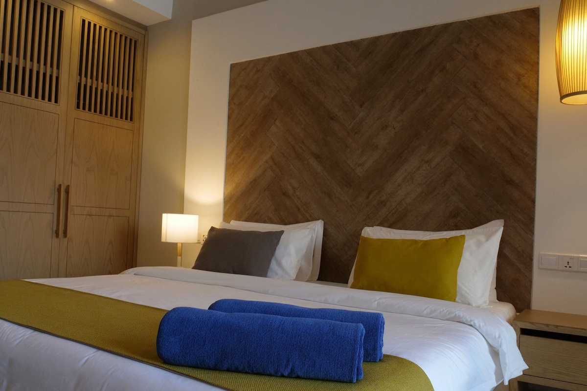A hotel room with a large bed, wooden headboard, and a nightstand with a lamp.
